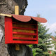 Roter Florfliegenkasten aus Holz mit schrägem Dach, befestigt an einem Baumstamm im Garten