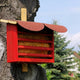 Roter Florfliegenkasten aus Holz mit schrägem Dach, befestigt an einem Baumstamm im Garten